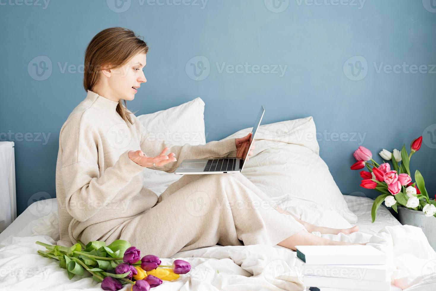 Mujer sentada en la cama en pijama charlando en el portátil foto