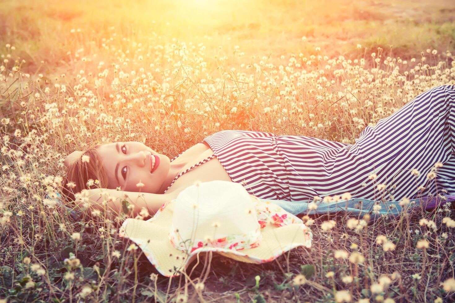 Young sexy woman lying in grass nearing her hat and smiley to camera photo