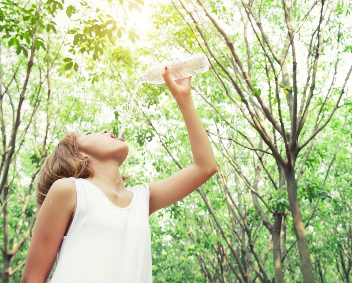 Young woman wearing white dress drinking water in the green forest. photo