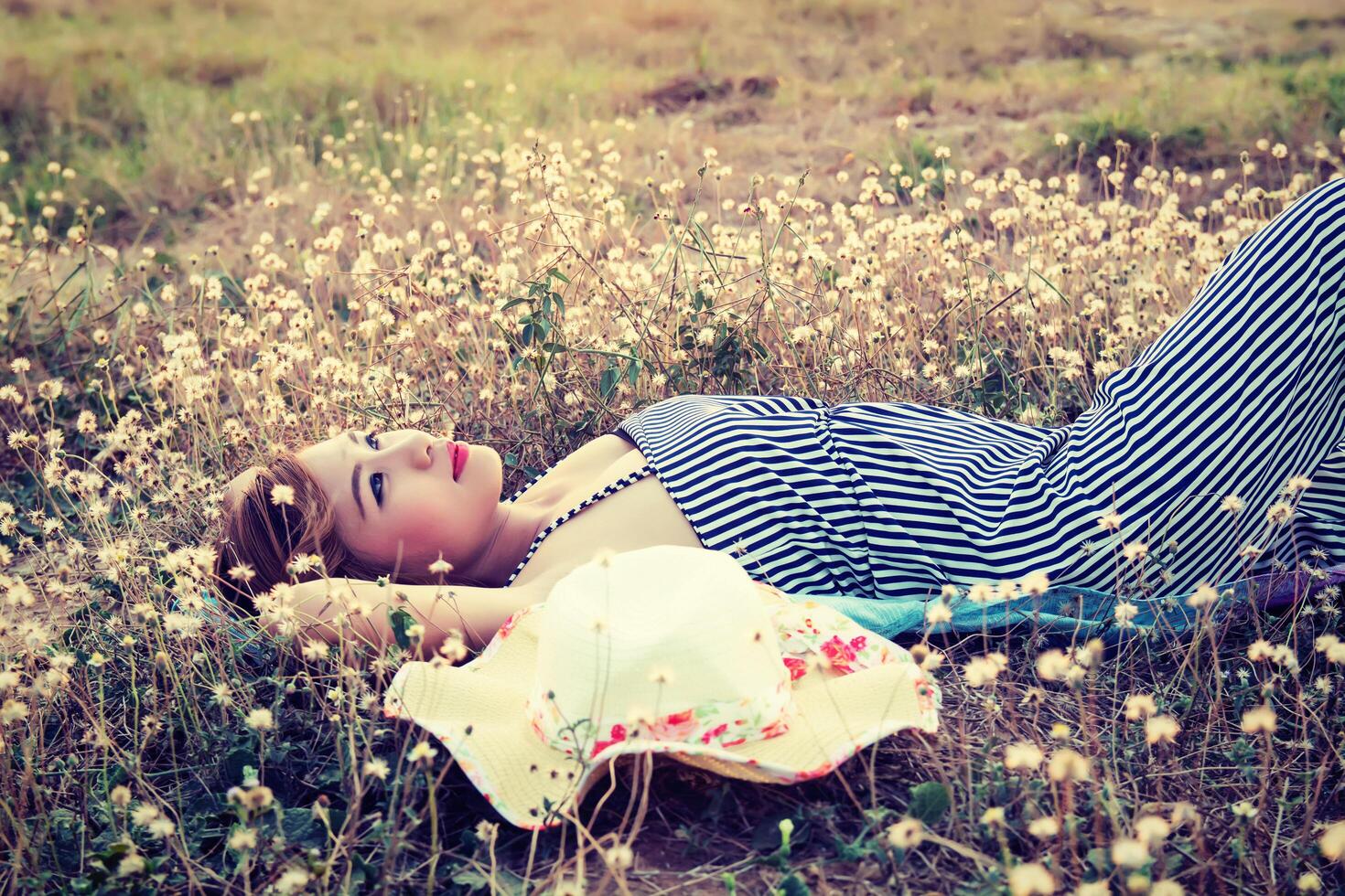 Young sexy woman lying in grass nearing her hat look into the sky photo