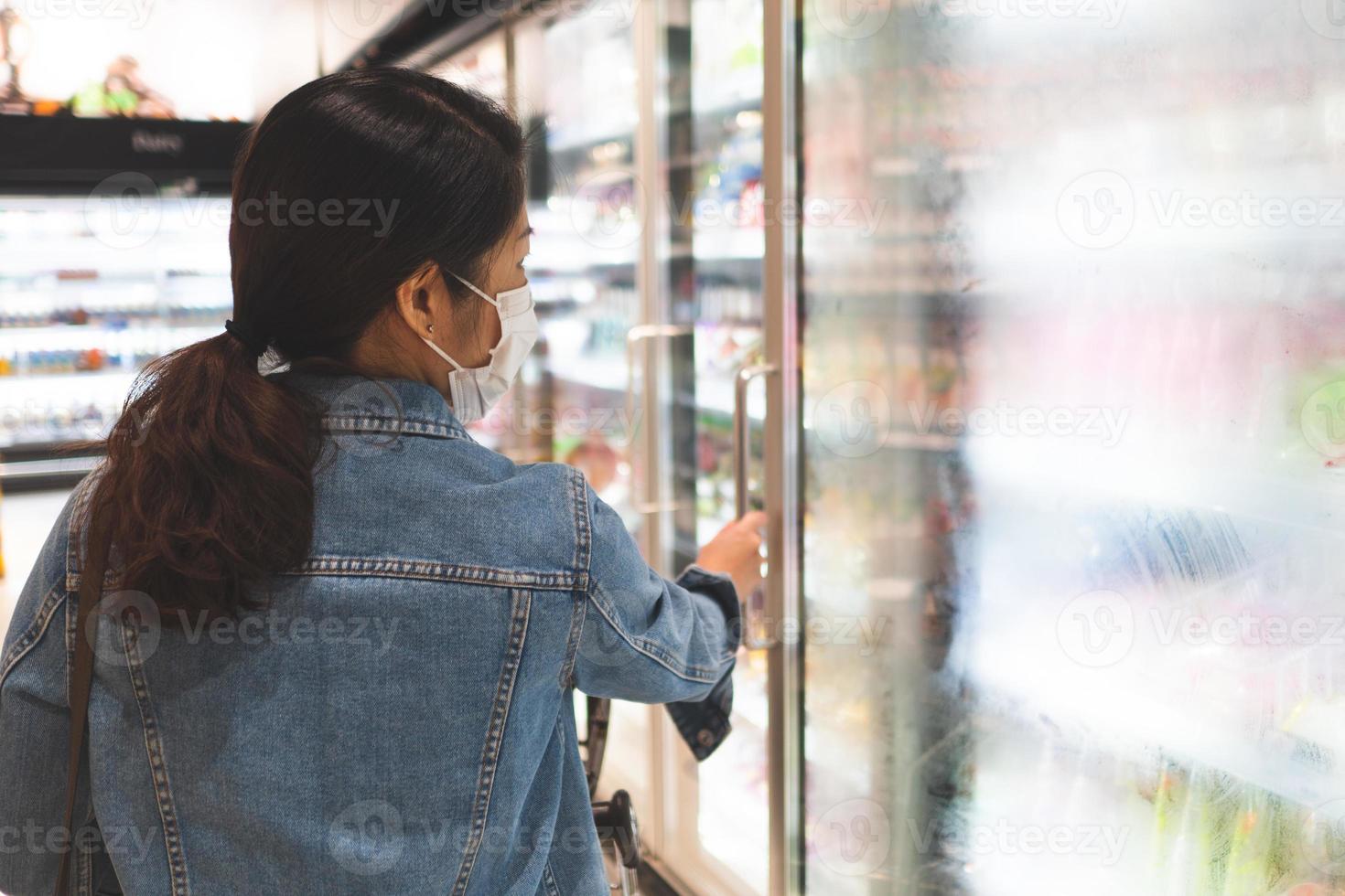 young woman wearing mask while shopping food in supermarket photo