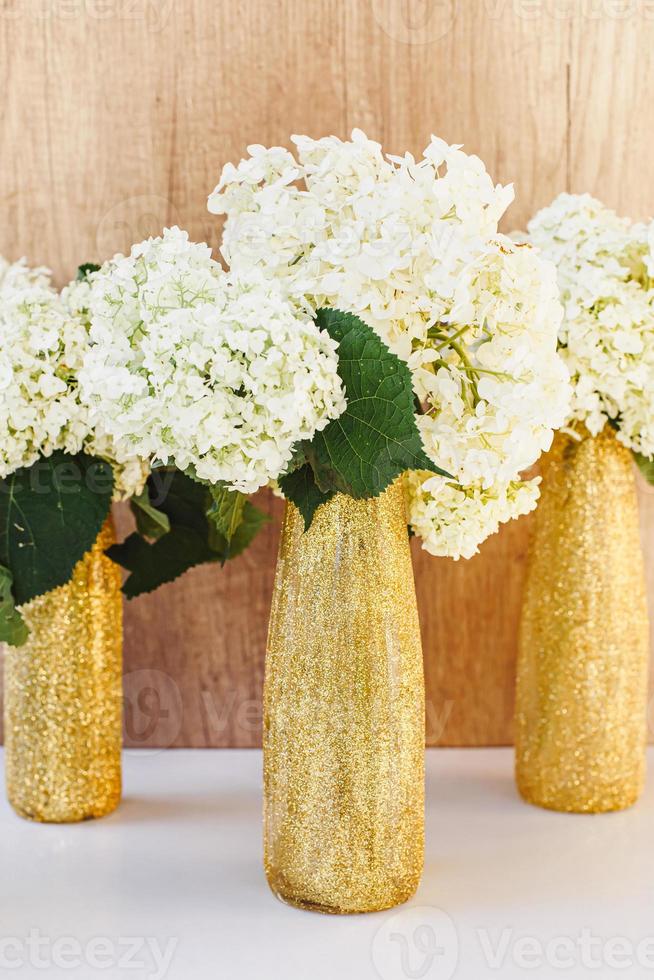 Golden glittered bottles with hydrangea. White flowers in gold vases photo