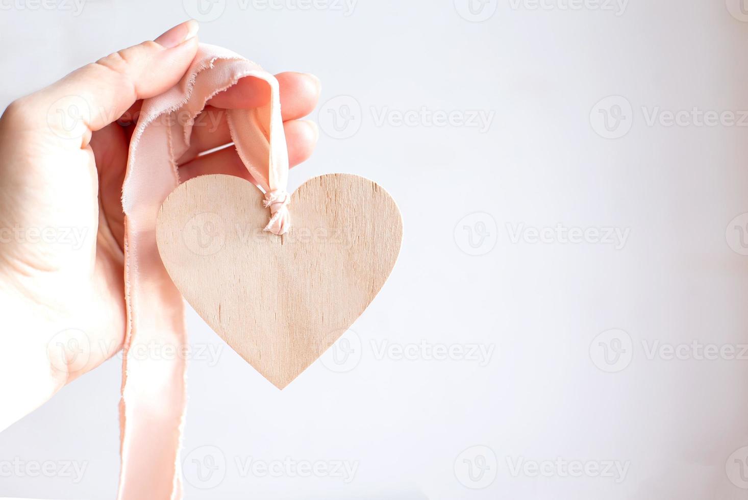 Wooden heart on pink ribbon. Hand holding wooden heart. Copy space. photo