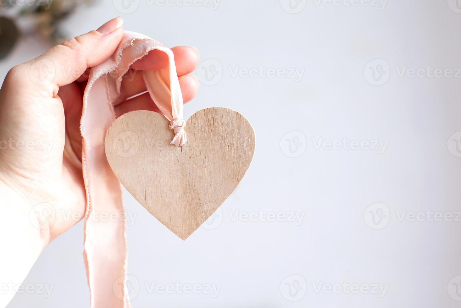 Wooden heart on pink ribbon. Hand holding wooden heart. Copy space. photo