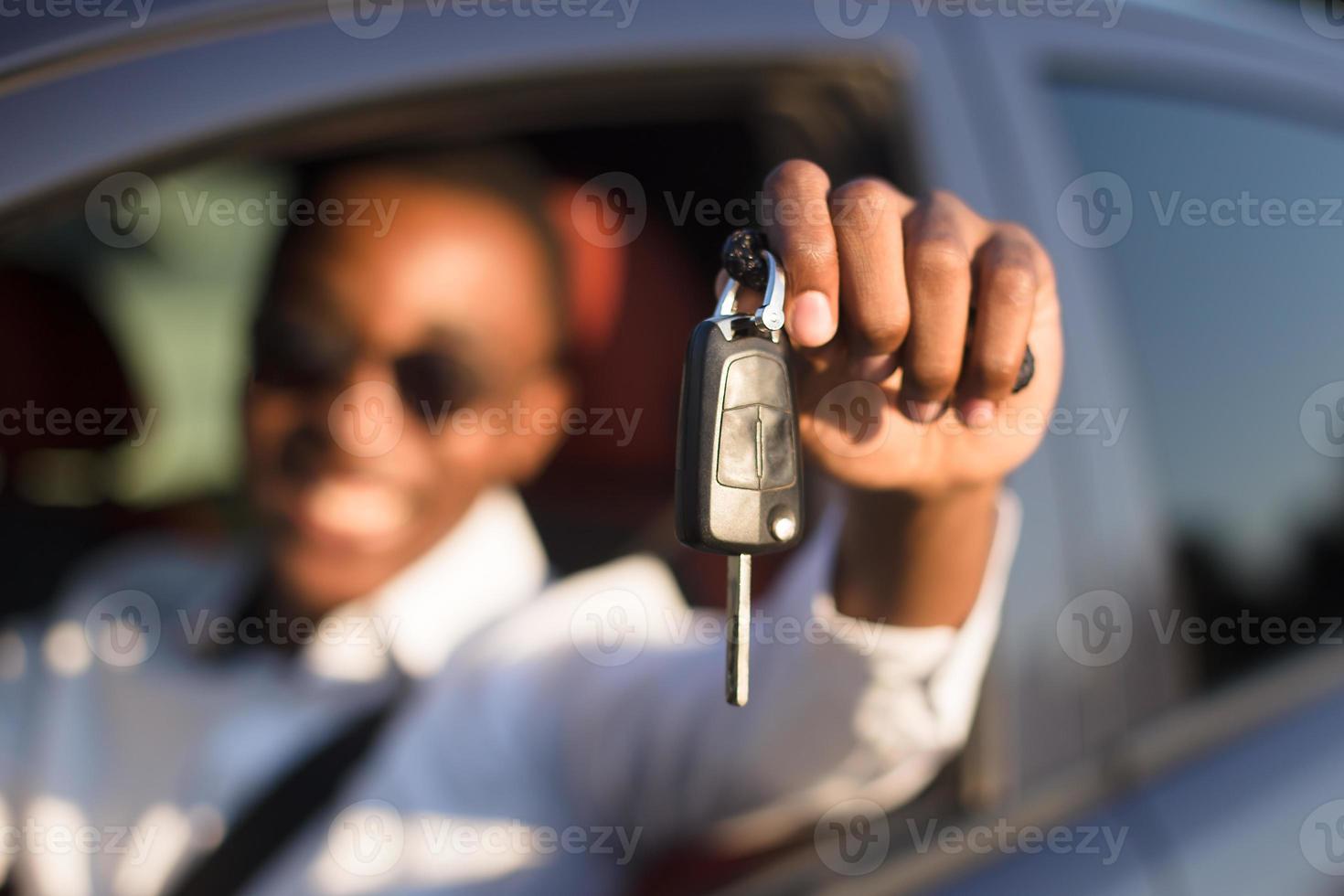 Afroamericano feliz en un coche con llave, en el verano foto