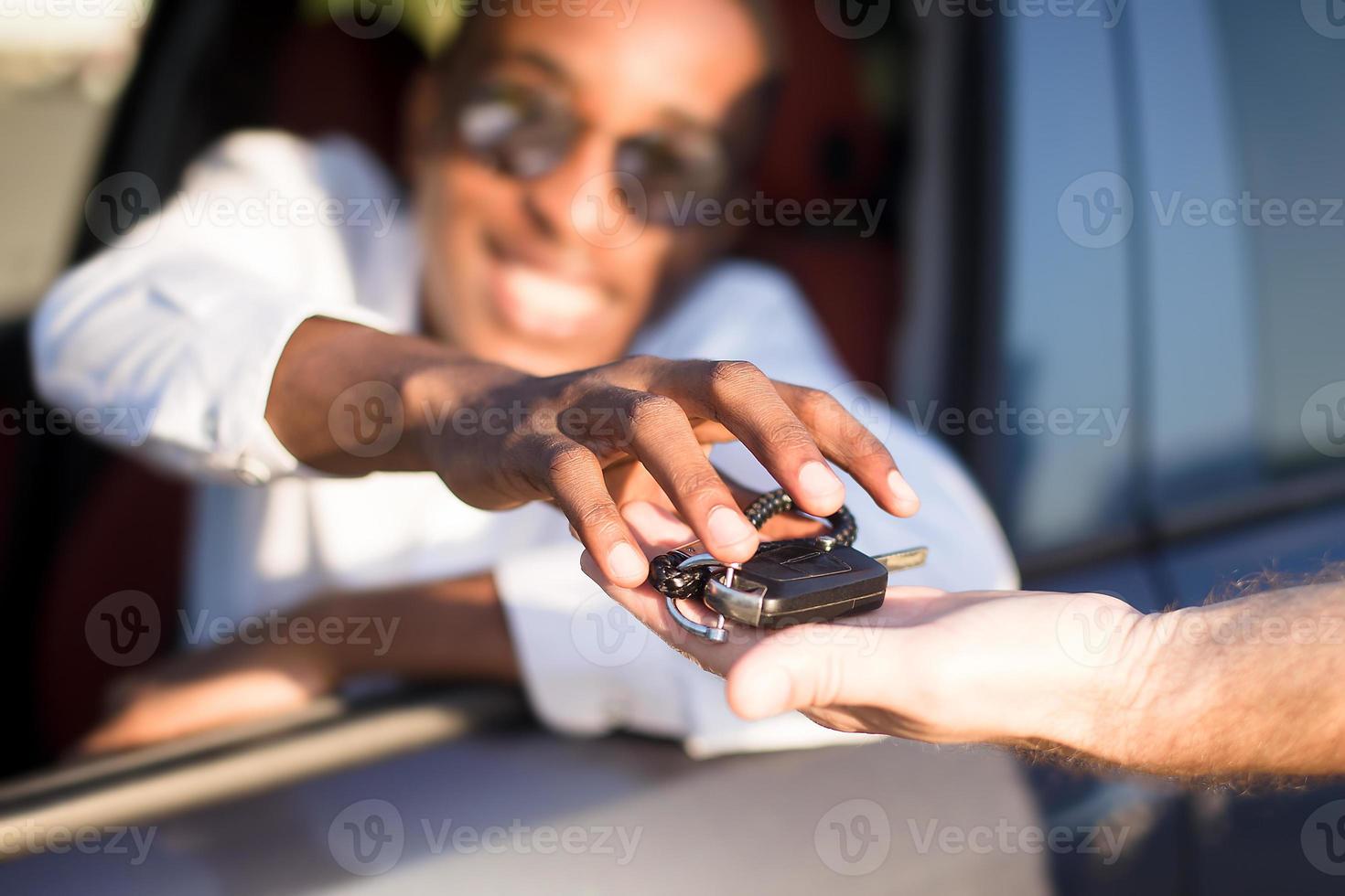 Afroamericano feliz en un coche con llave, en el verano foto