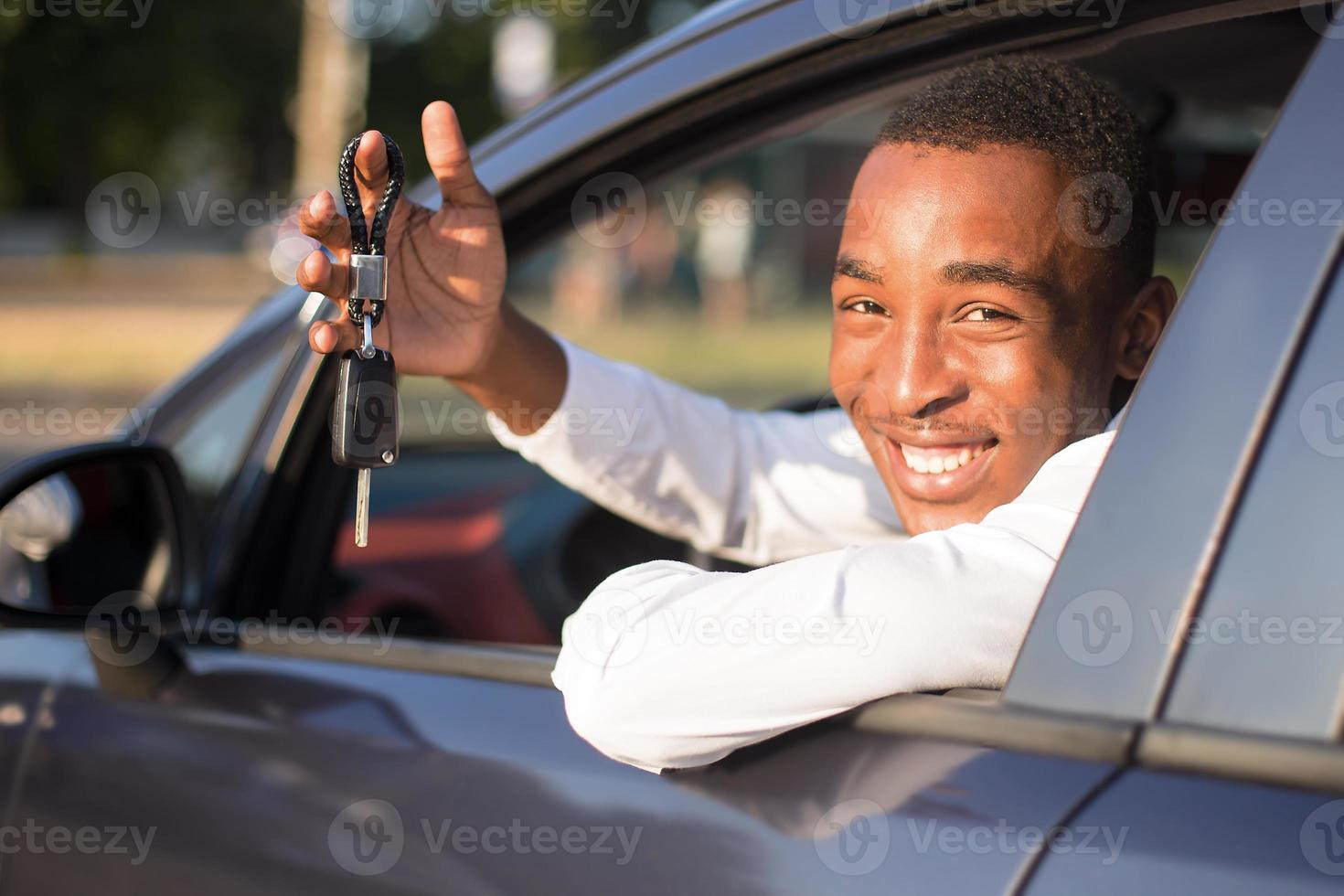 Afroamericano feliz en un coche con llave, en el verano foto