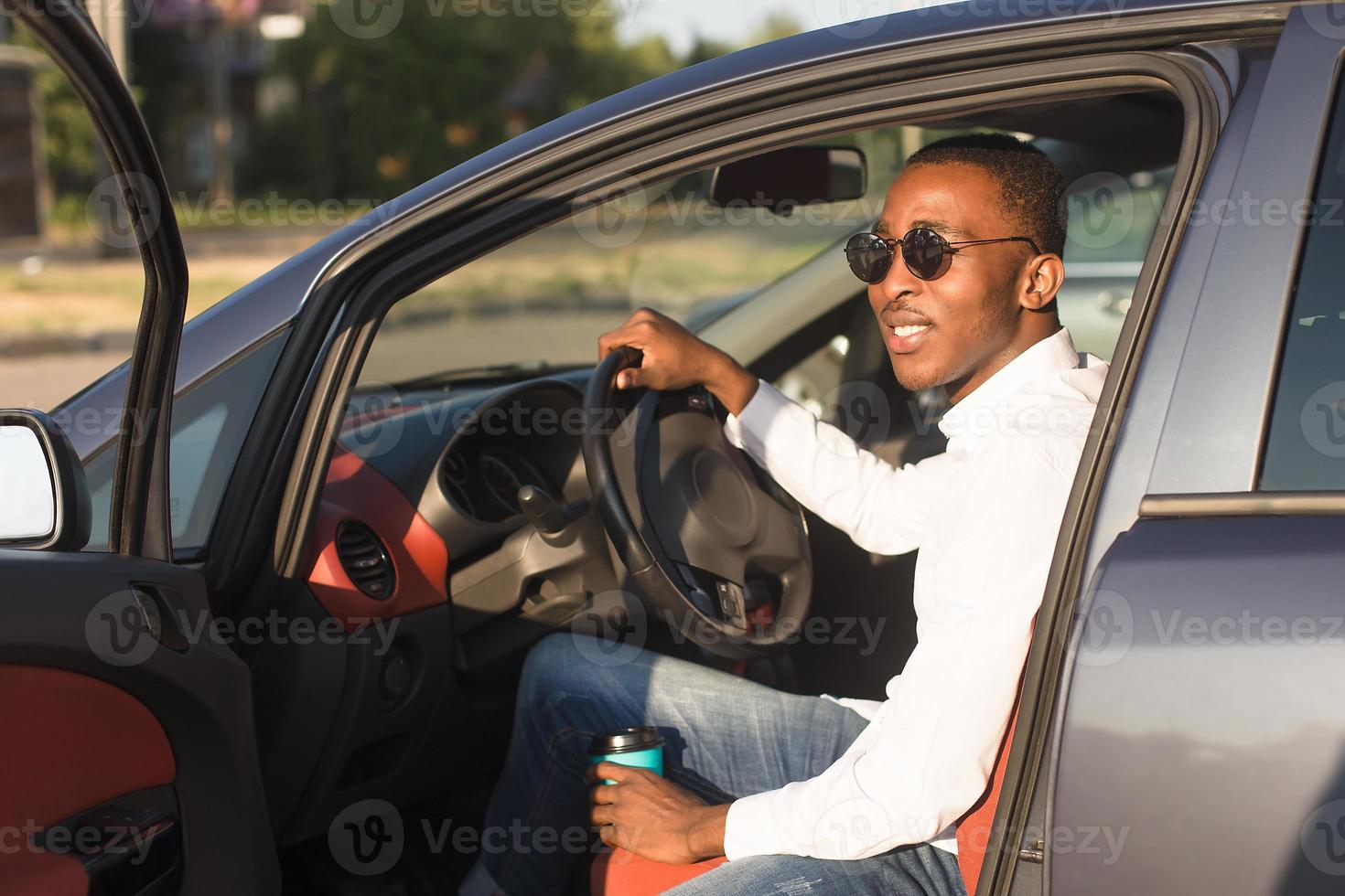 Feliz afroamericano conduciendo un coche con café, en el verano foto