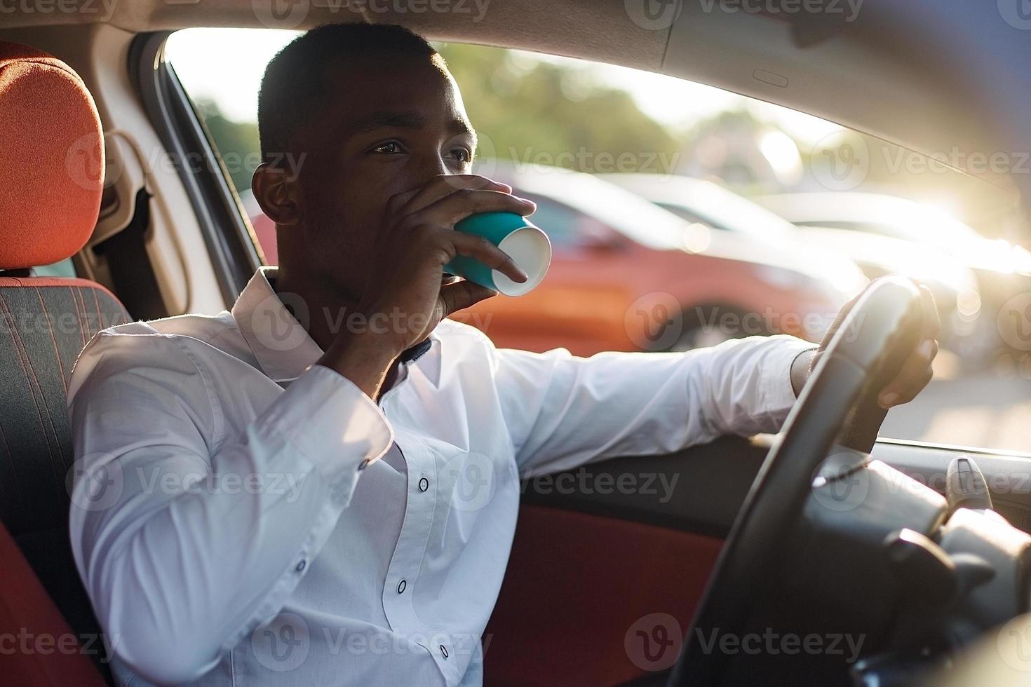 Feliz afroamericano conduciendo un coche con café, en el verano foto