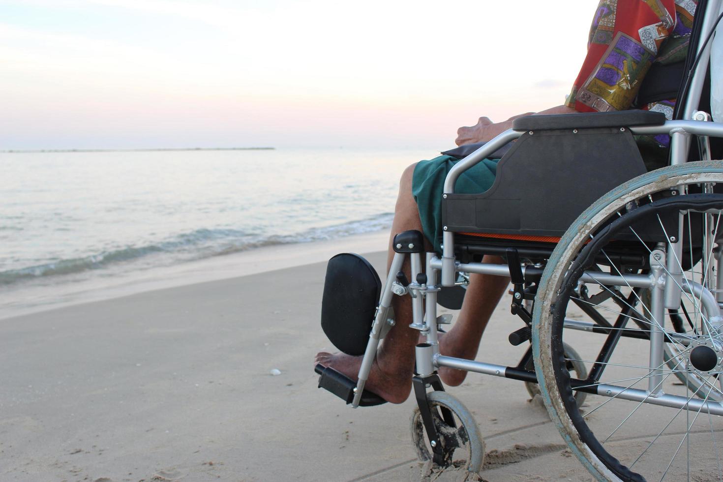 old man on a wheelchair looks at the sea from the beach photo