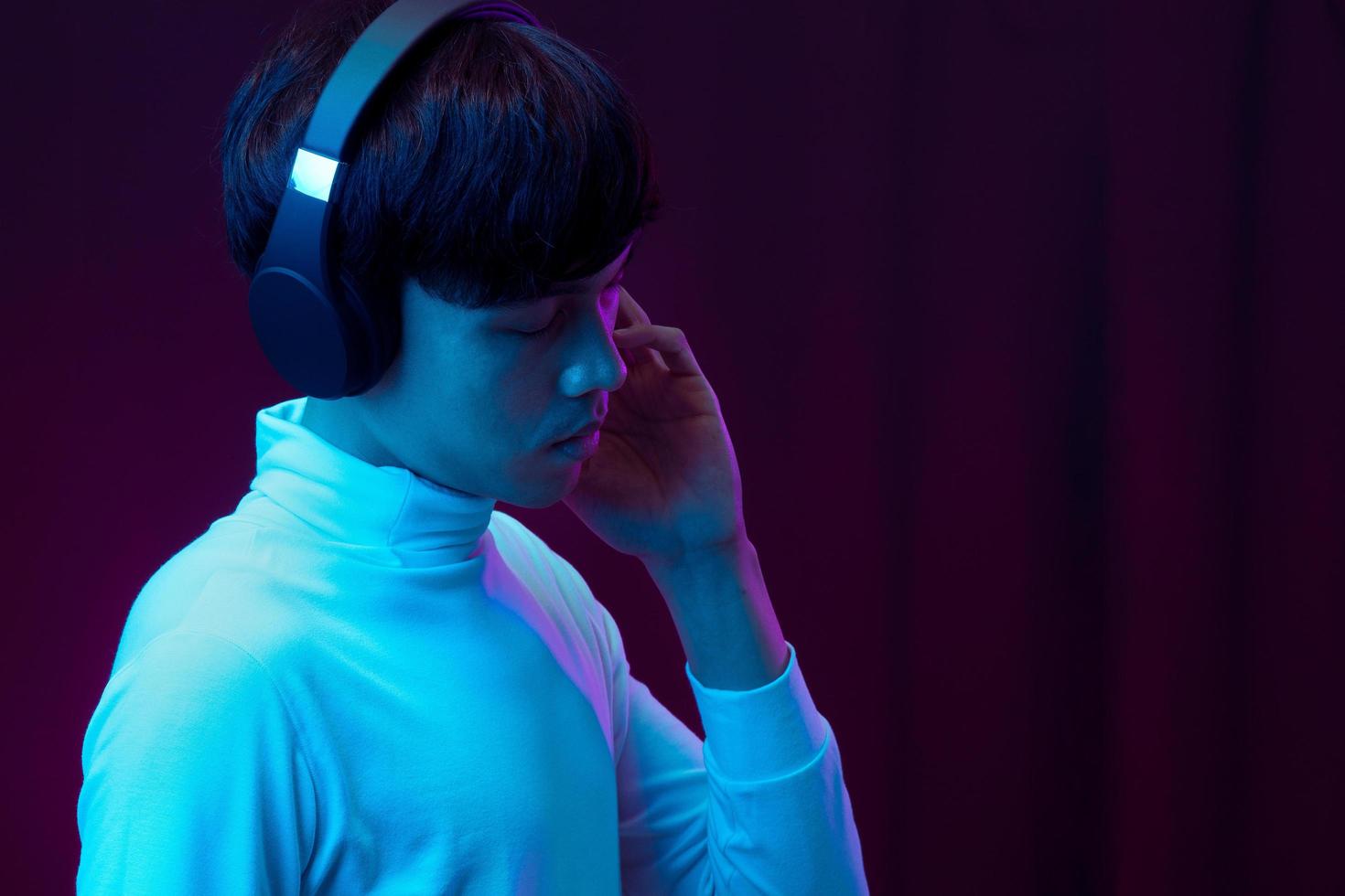 Joven asiático escuchando música con auriculares en luz de neón foto