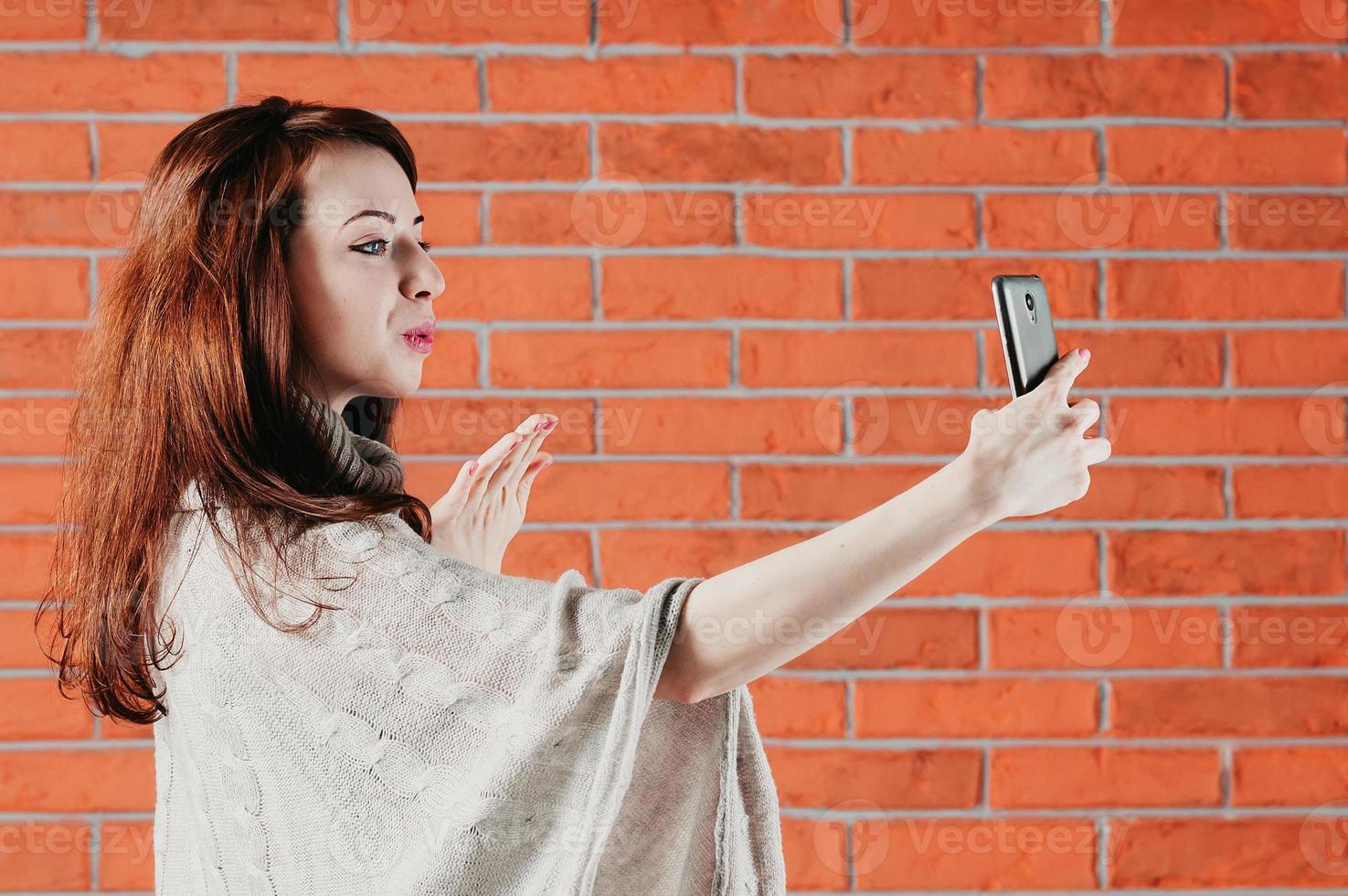 una chica guapa está haciendo selfie con teléfono inteligente, enviando beso al aire foto