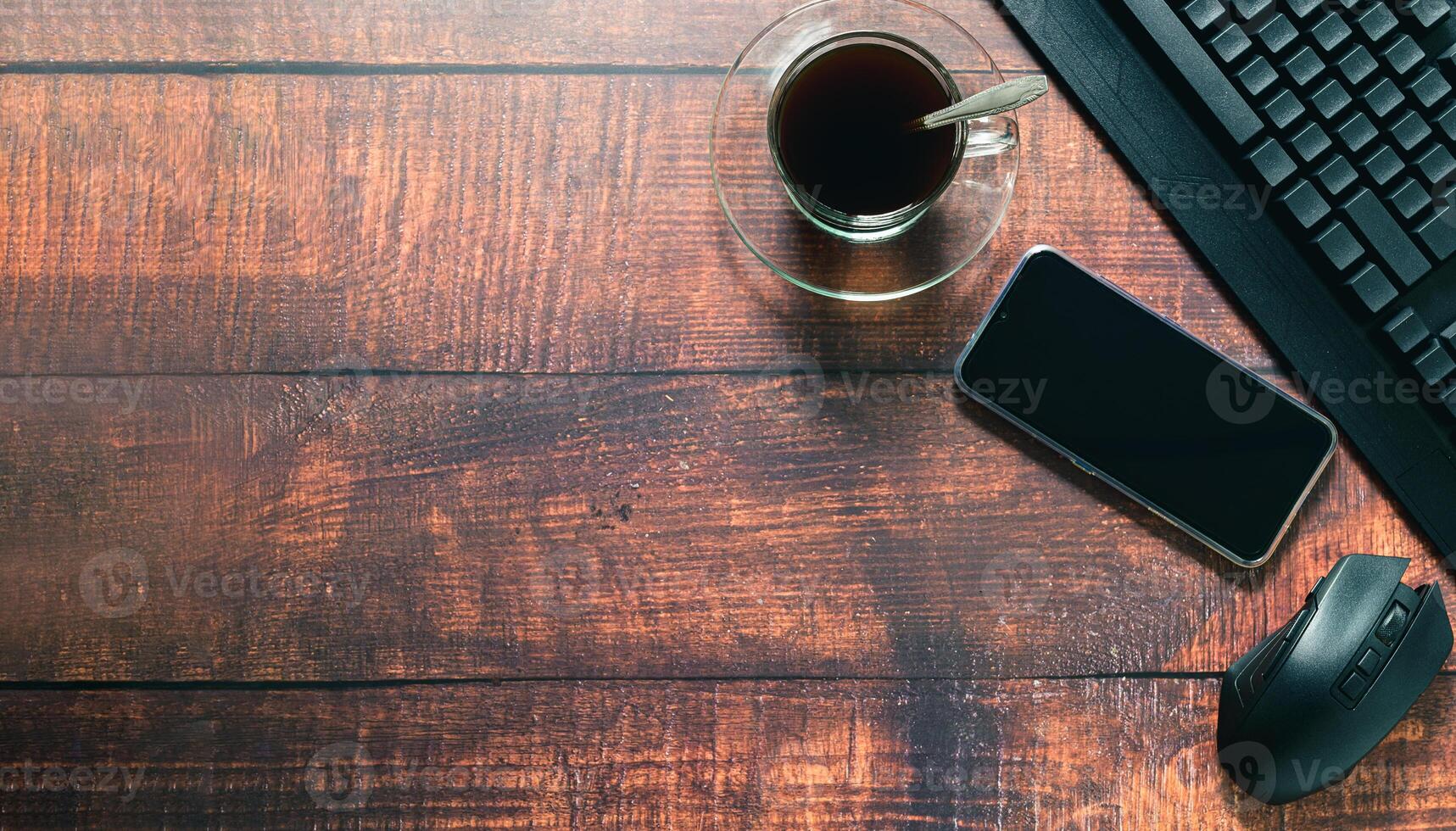 A coffee cup, a smartphone and a keyboard on a wooden desk photo