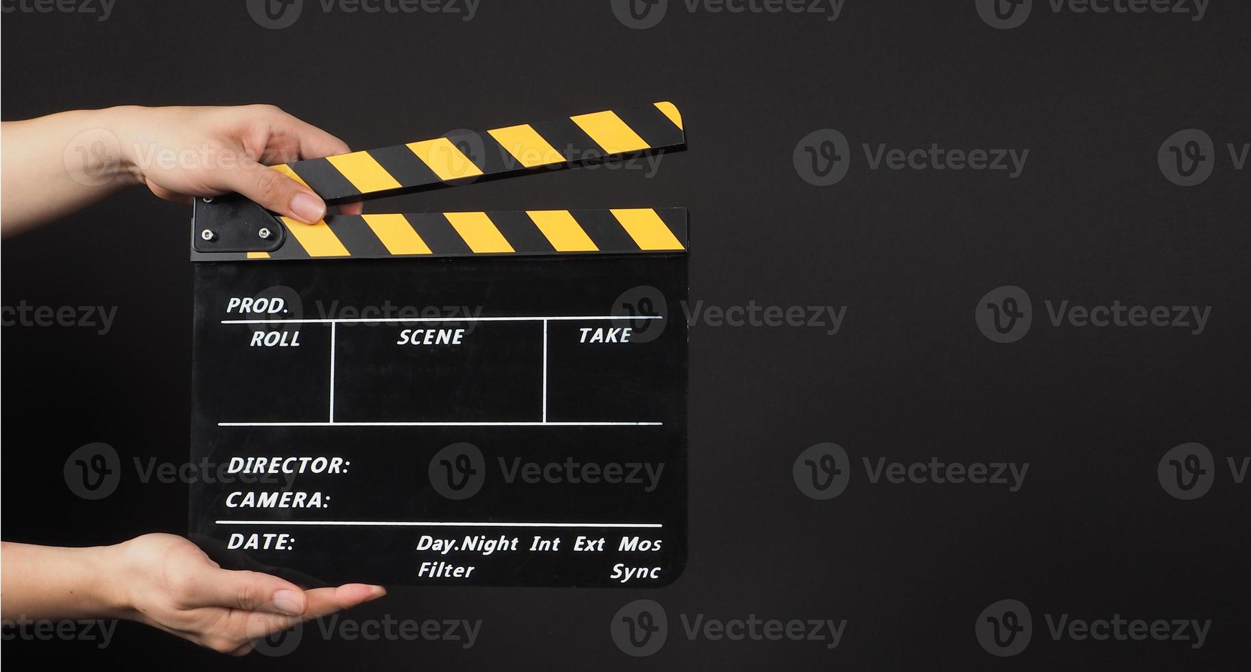 Hand is holding yellow and black clapperboard on black background. photo