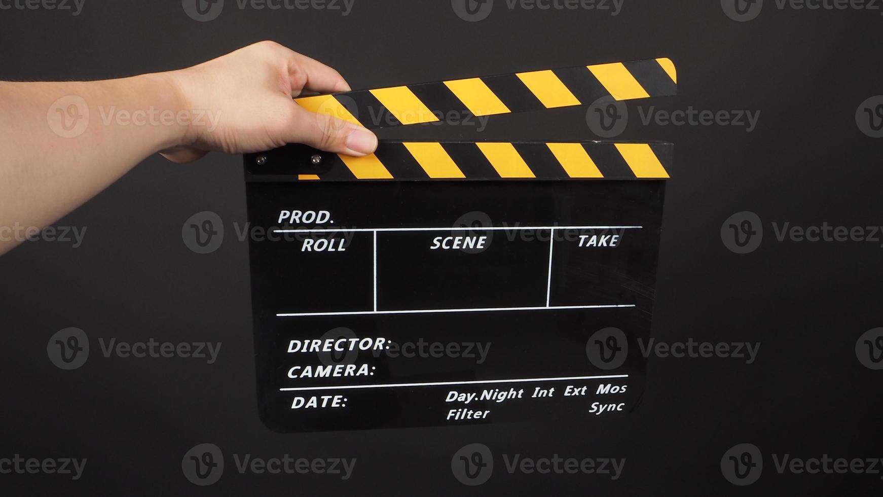 Hand is hold yellow and black color clapperboard on black background. photo