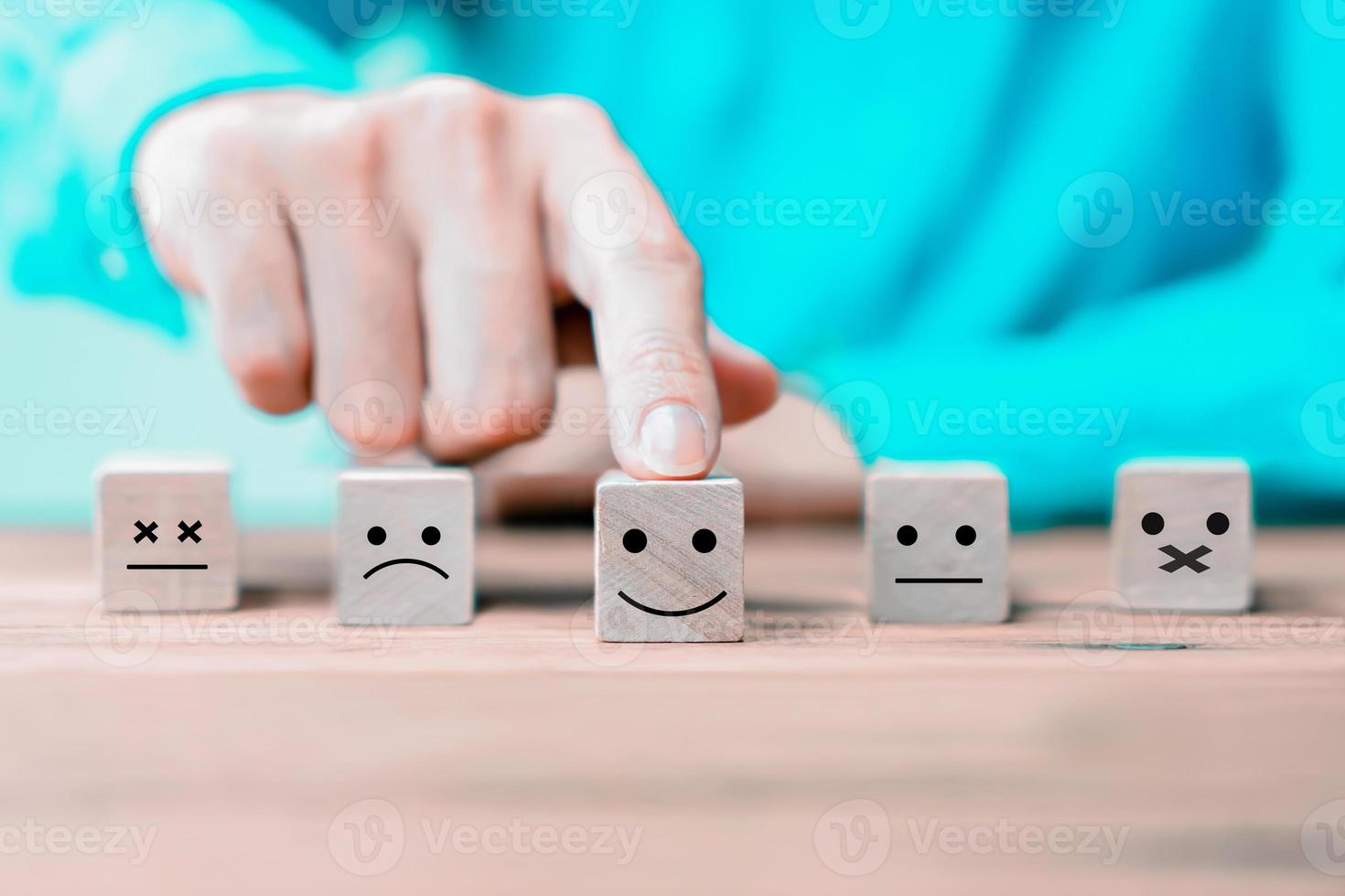 El empresario elige una cara de iconos de emoticonos felices en un bloque de madera. foto