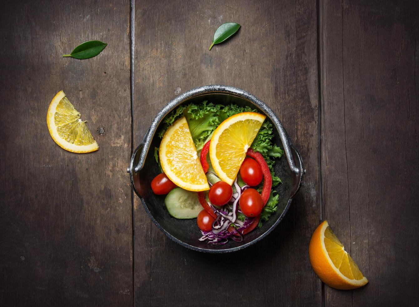 Ensalada de verduras frescas con naranja en la sartén sobre fondo de madera foto