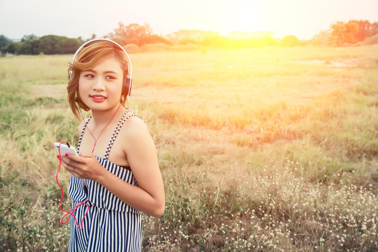 hermosa mujer escuchando música desde el teléfono inteligente en el campo de flores. foto