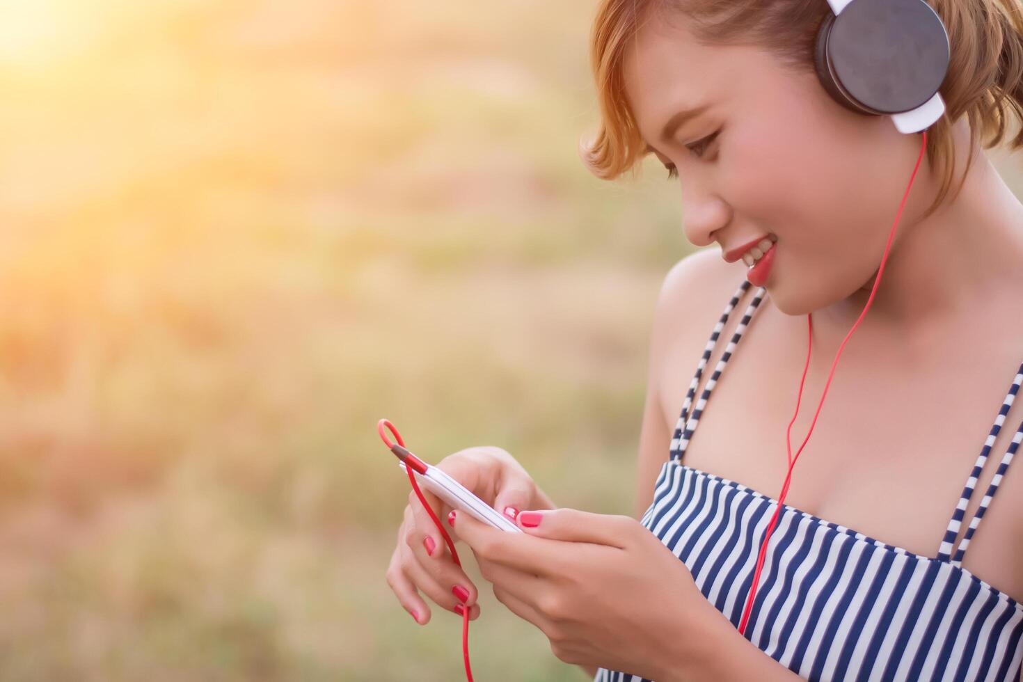 Hermosa mujer joven sexy acostada acercándose a los auriculares en el campo de flores foto