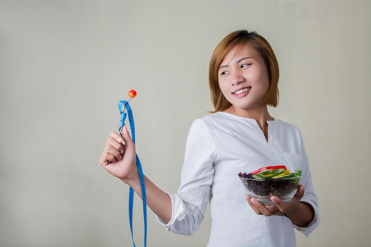 mujer de pie sosteniendo un tazón de ensalada mirando tenedor mojar tomate. foto