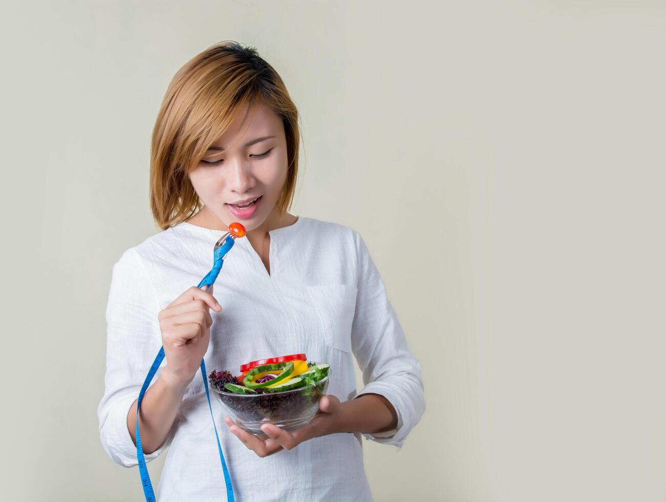 mujer sosteniendo tenedor con verduras frescas mixtas y cinta métrica. foto