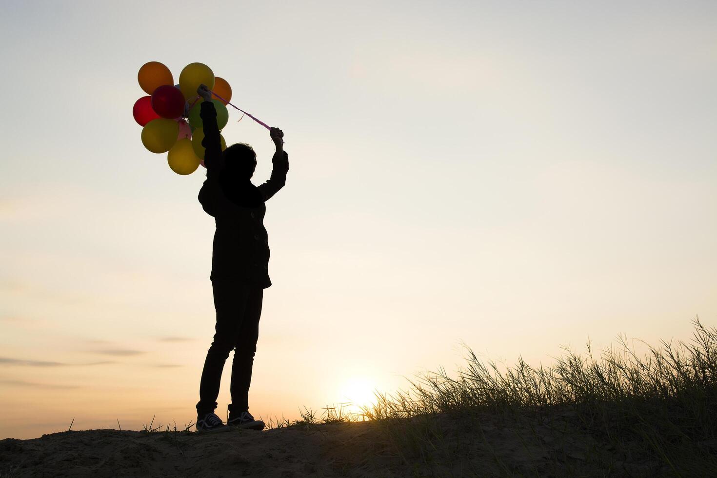 silueta, de, mujer joven, tenencia, colorido, de, globos, con, ocaso foto