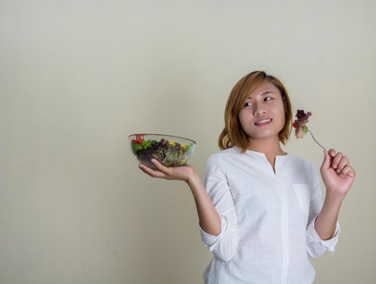 Bella mujer de pie sosteniendo un tazón de ensalada comiendo algunas verduras foto