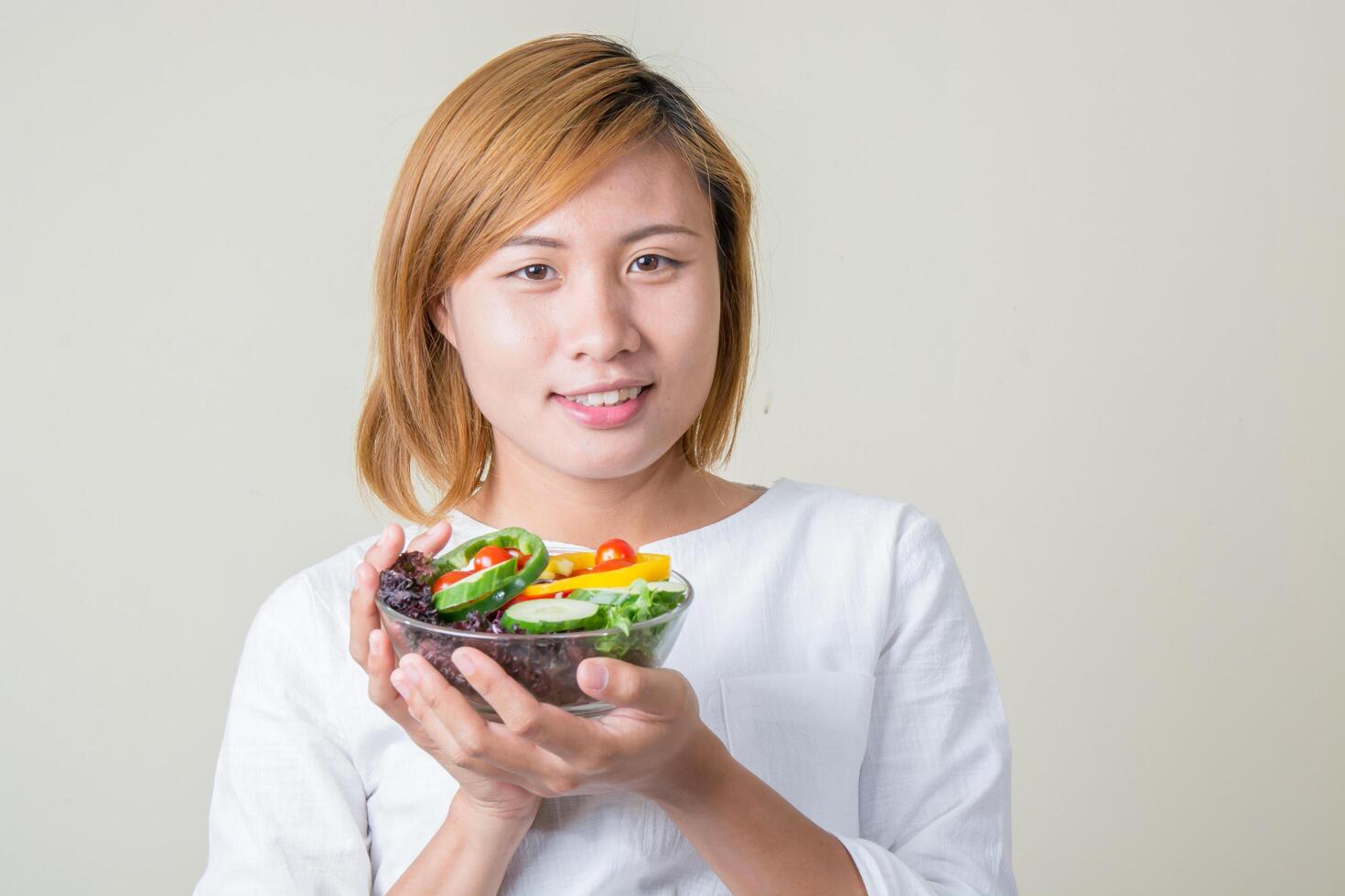 Beautiful woman holding bowl of fresh vegetable salad smiles at camera photo