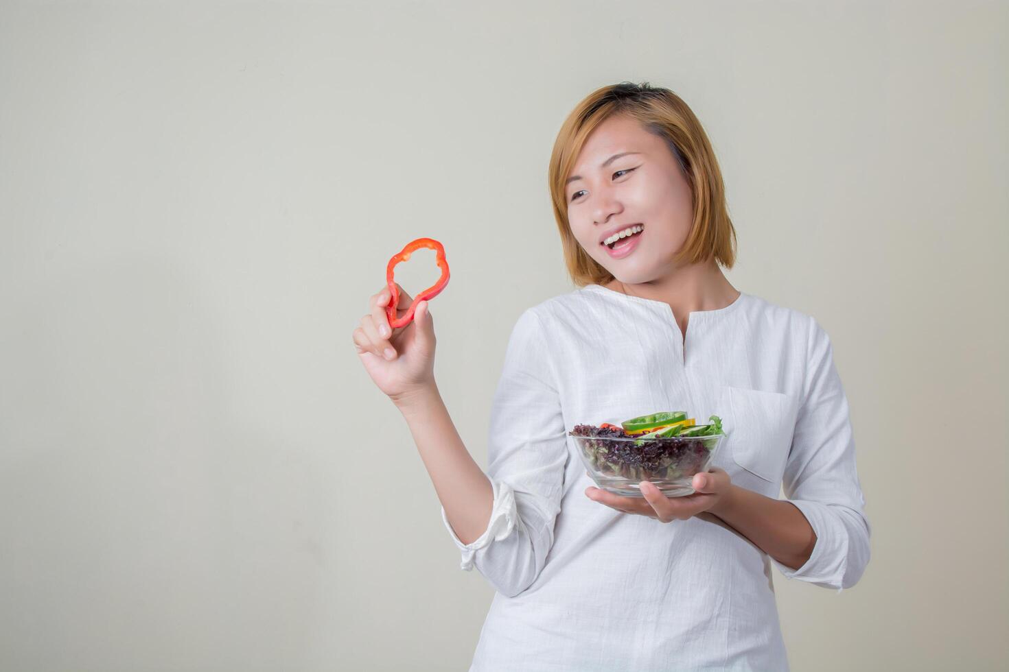 Bella mujer de pie sosteniendo un tazón de ensalada comiendo algunas verduras foto