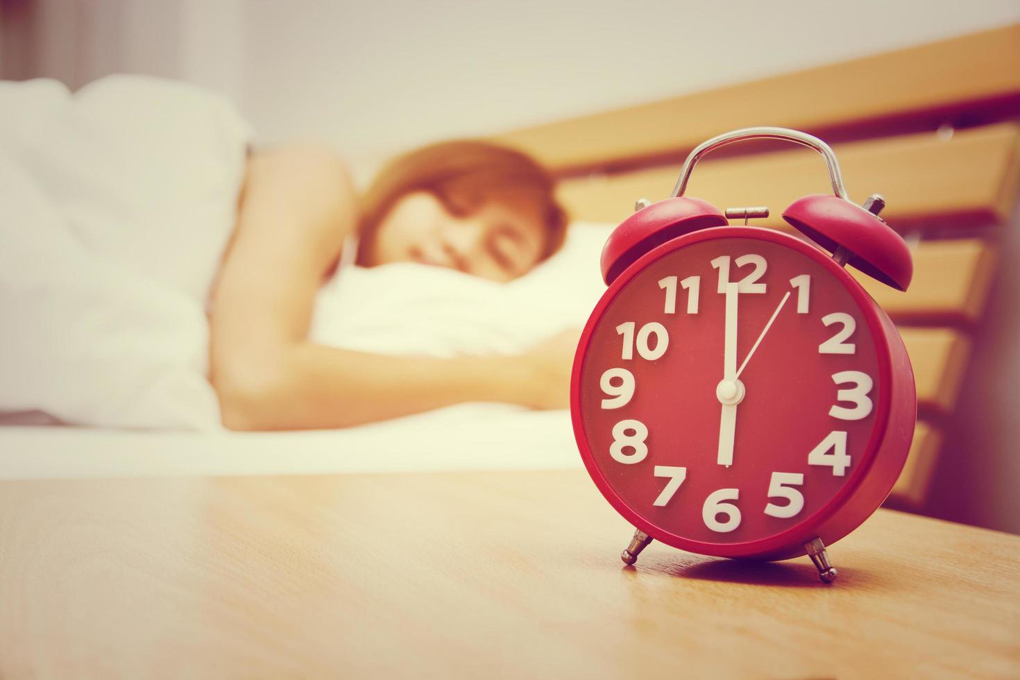 mujer durmiendo en la cama con despertador rojo por la mañana. foto