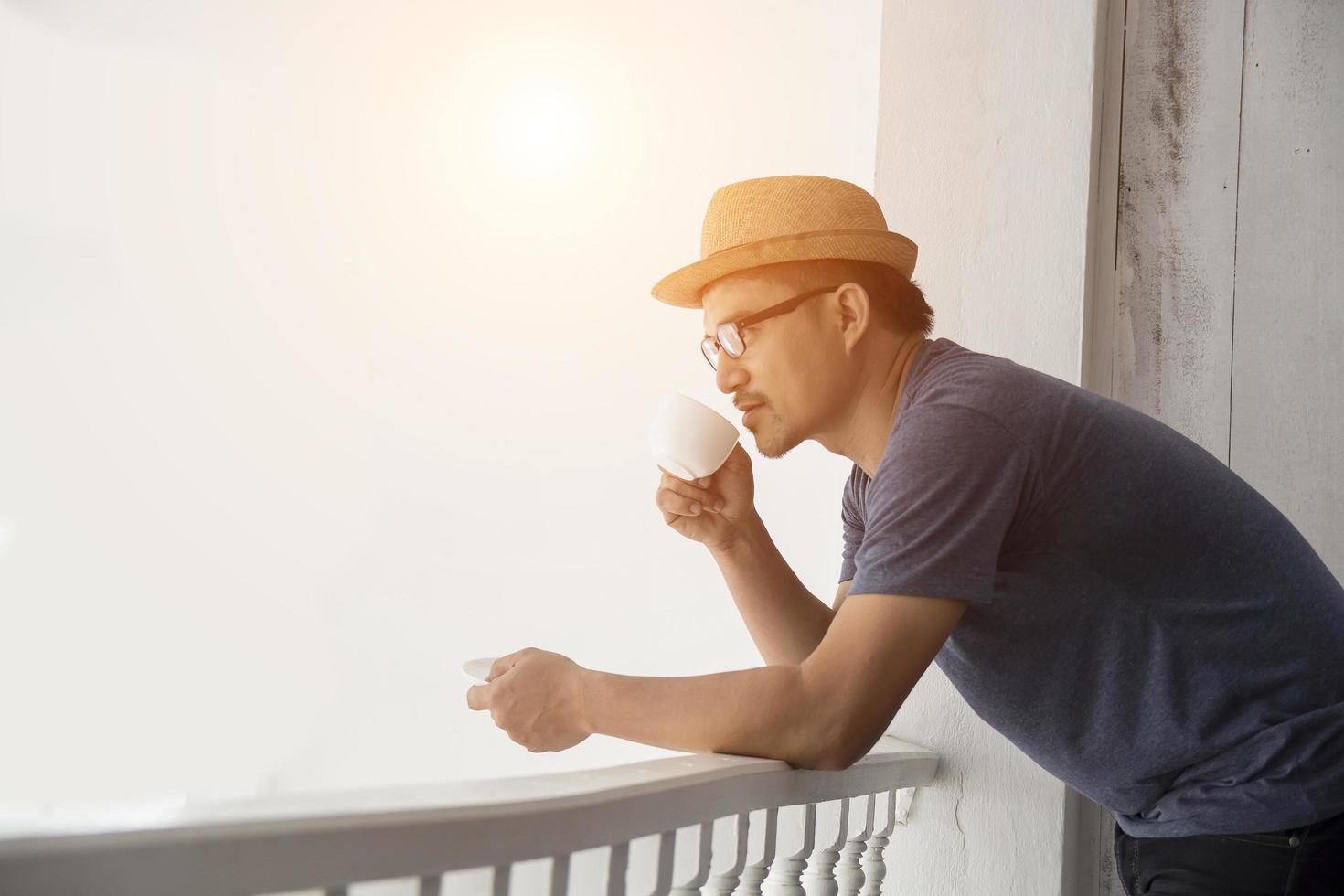 Hombre joven inconformista descansando en el balcón de su casa con la salida del sol foto