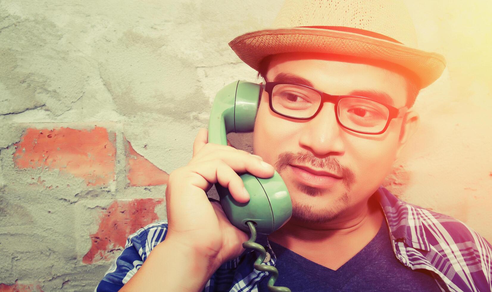 handsome hipster man talking with retro phone on the brick background photo