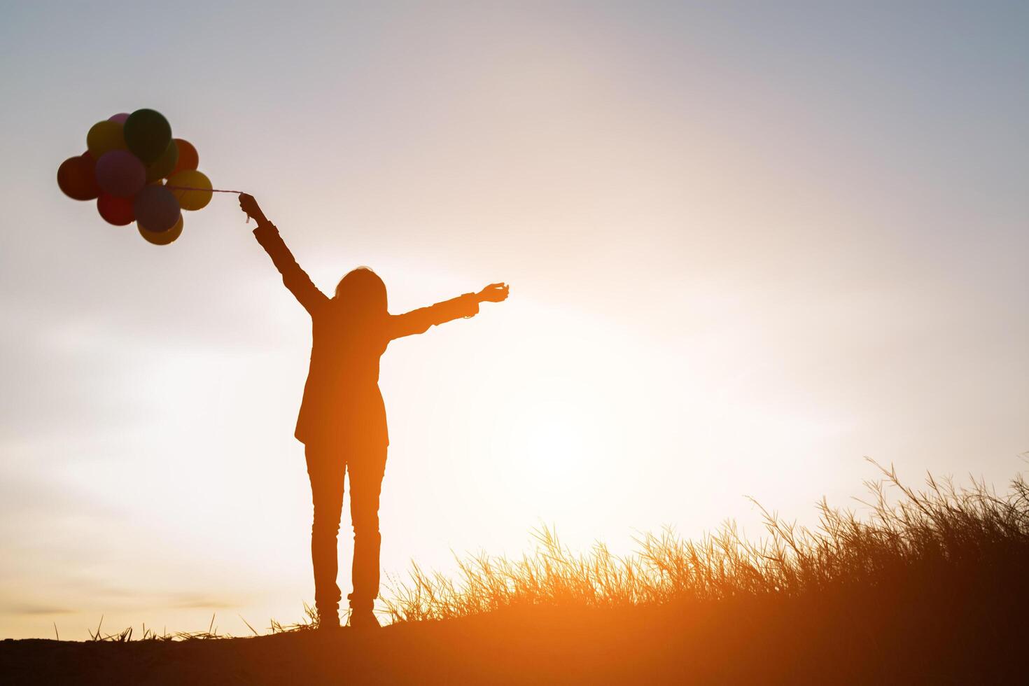 silueta, de, mujer joven, tenencia, colorido, de, globos, con, ocaso foto