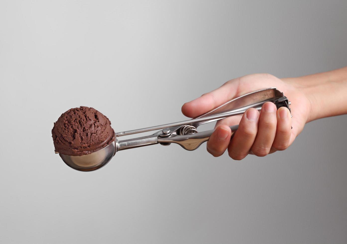 Hand holding chocolate ice cream in spoon for scoop on gray background photo