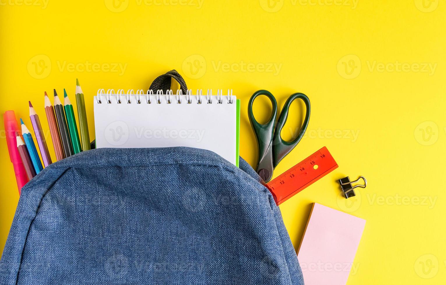 Mochila escolar con material de oficina sobre fondo amarillo foto