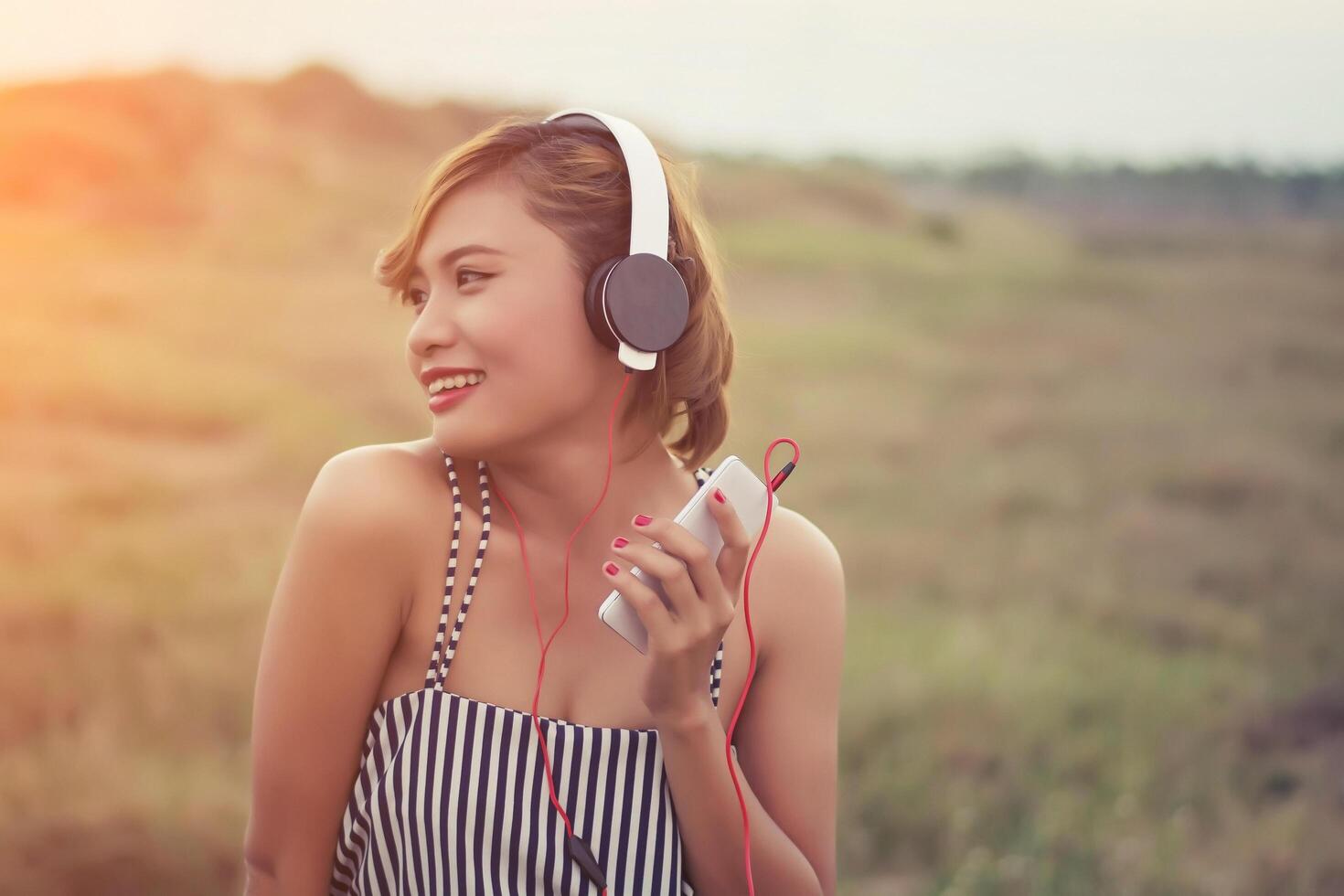 Hermosa mujer joven sexy acostada acercándose a los auriculares en el campo de flores foto