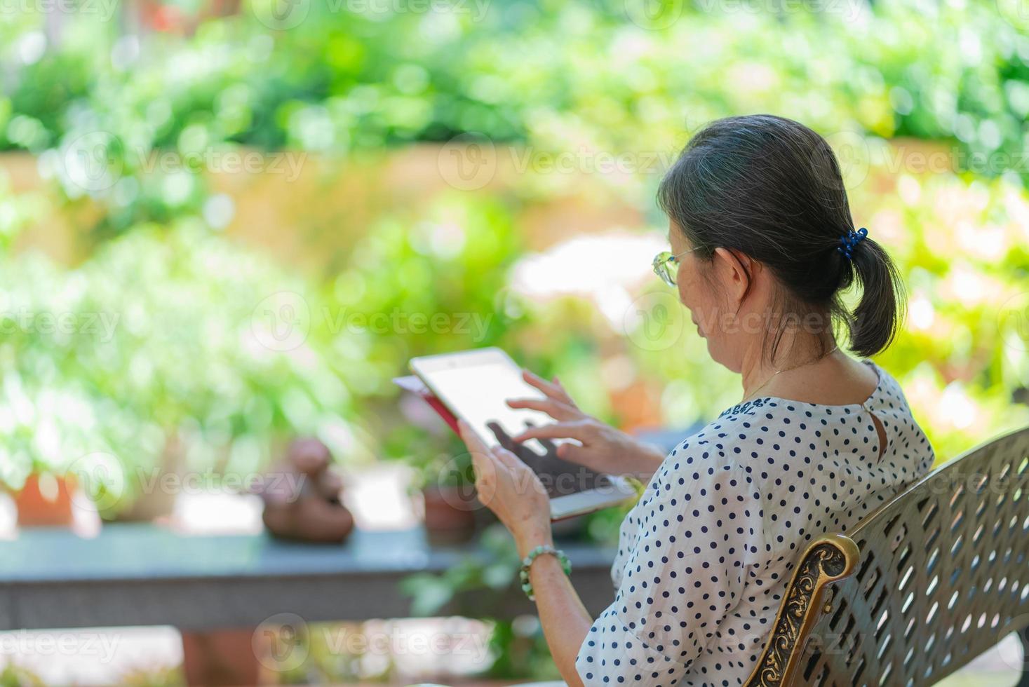 Mujer asiática mayor que usa la tableta para reproducir las redes sociales en el jardín de su casa. foto