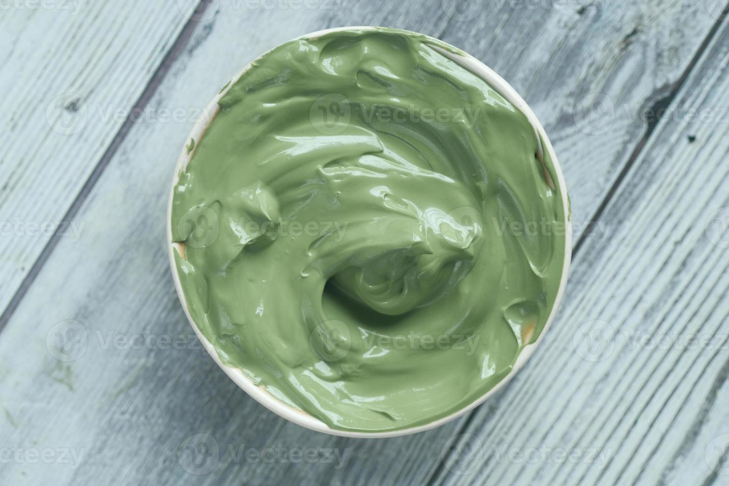 green clay mask in container on wooden background photo