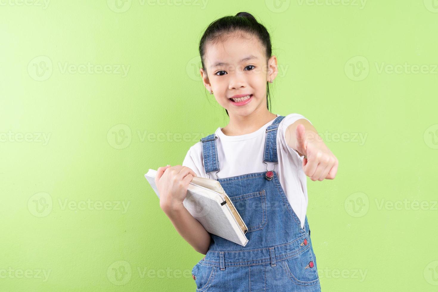 Portrait of Asian child holding book on green background photo