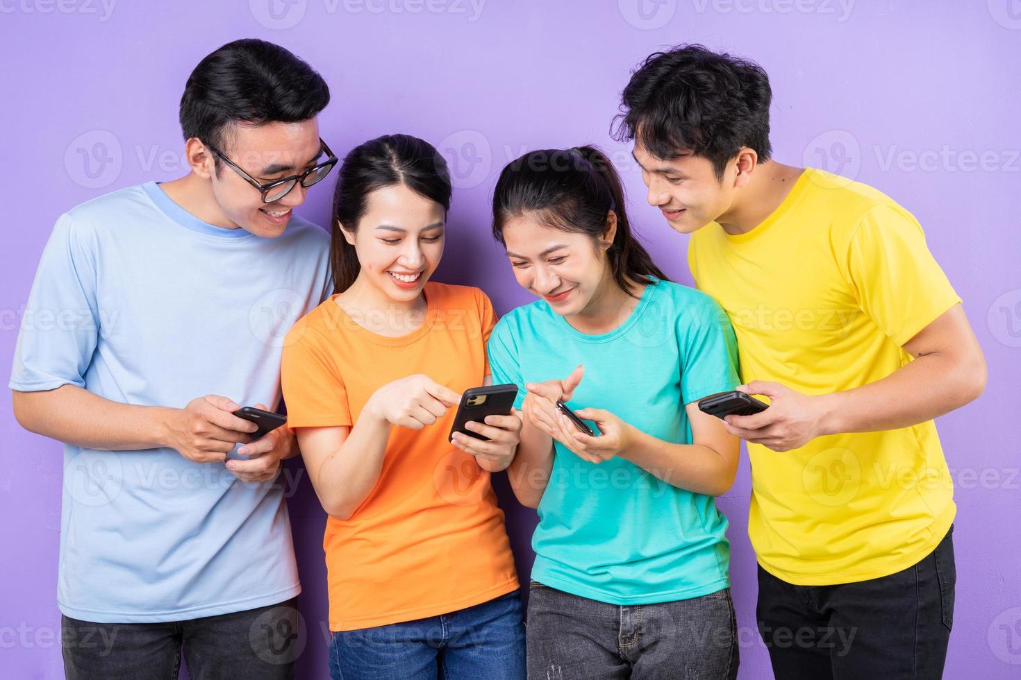 Grupo de mejores amigos asiáticos mediante teléfono celular sobre fondo púrpura foto