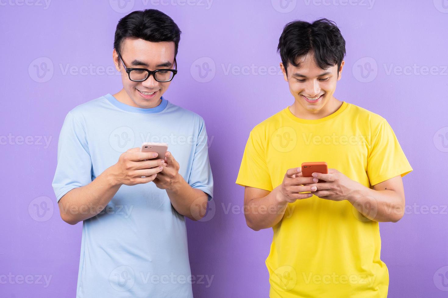 Two Asian brothers using cell phones on purple background photo