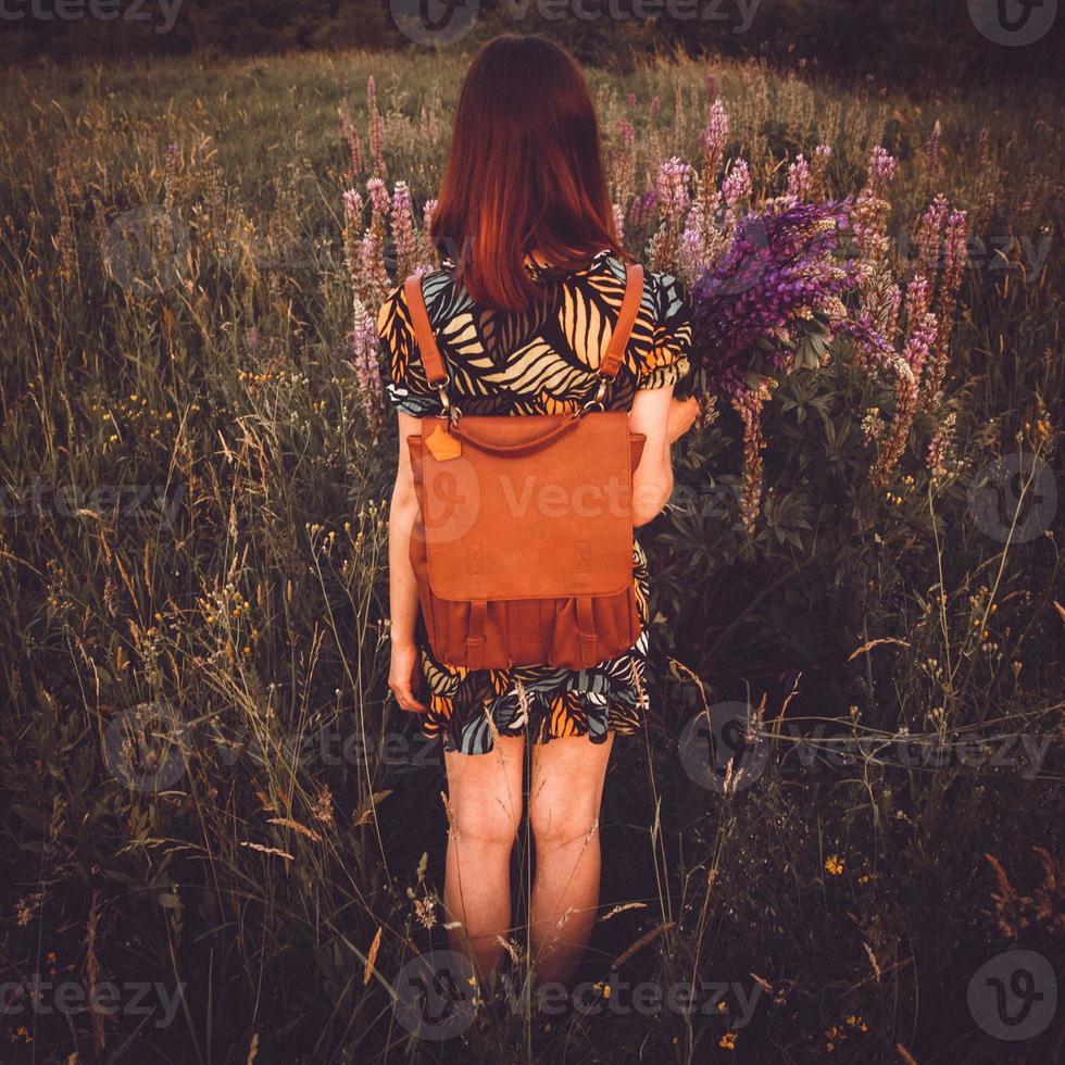 Girl standing in a field with flowers and a backpack photo