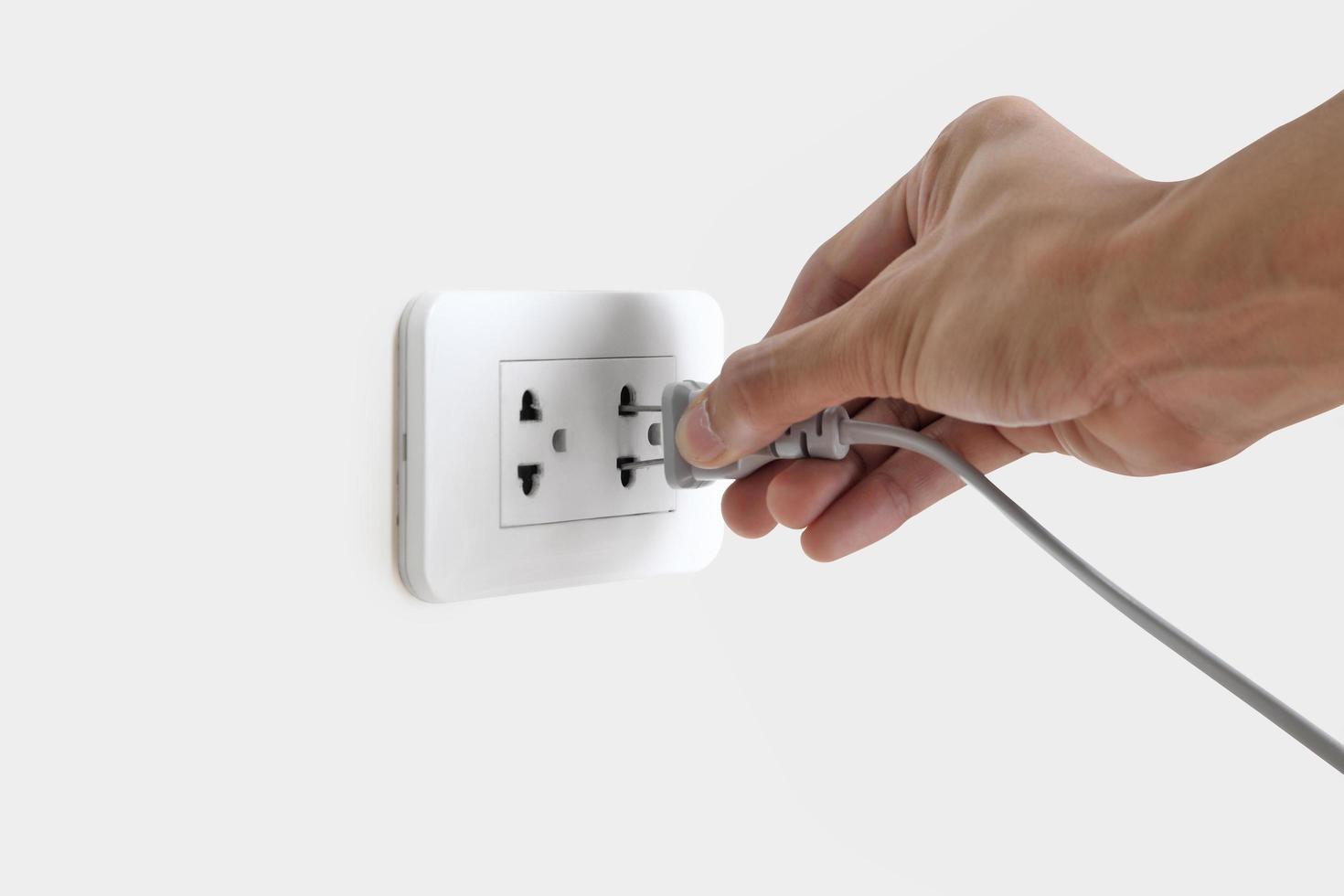 Hand plugging in electric cord to a white socket photo