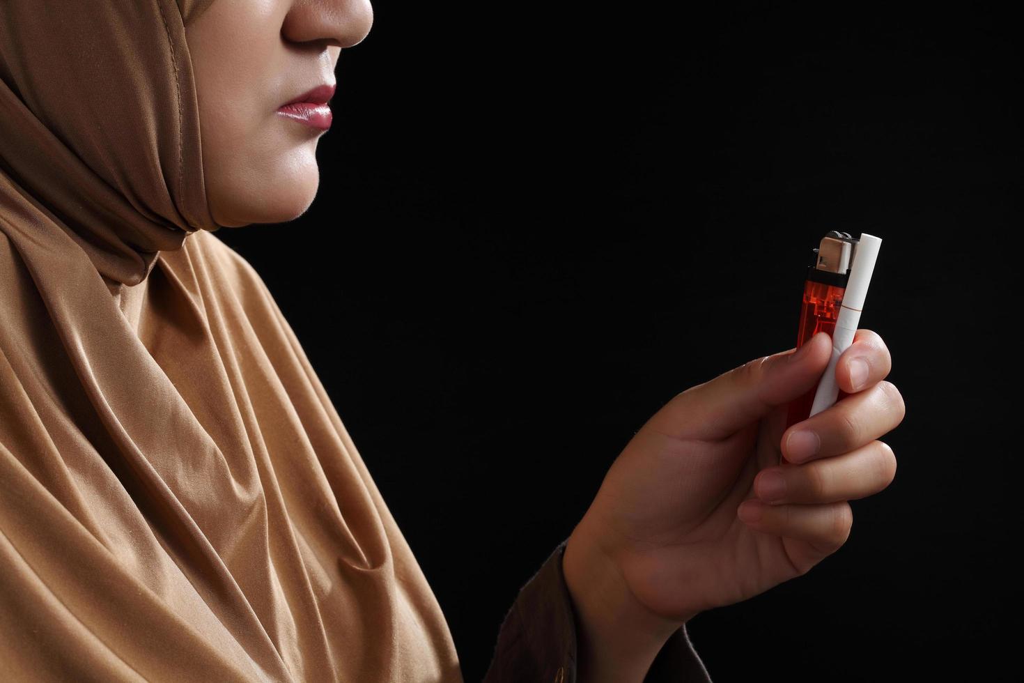 Close up young muslim woman holding a cigarette on black background photo
