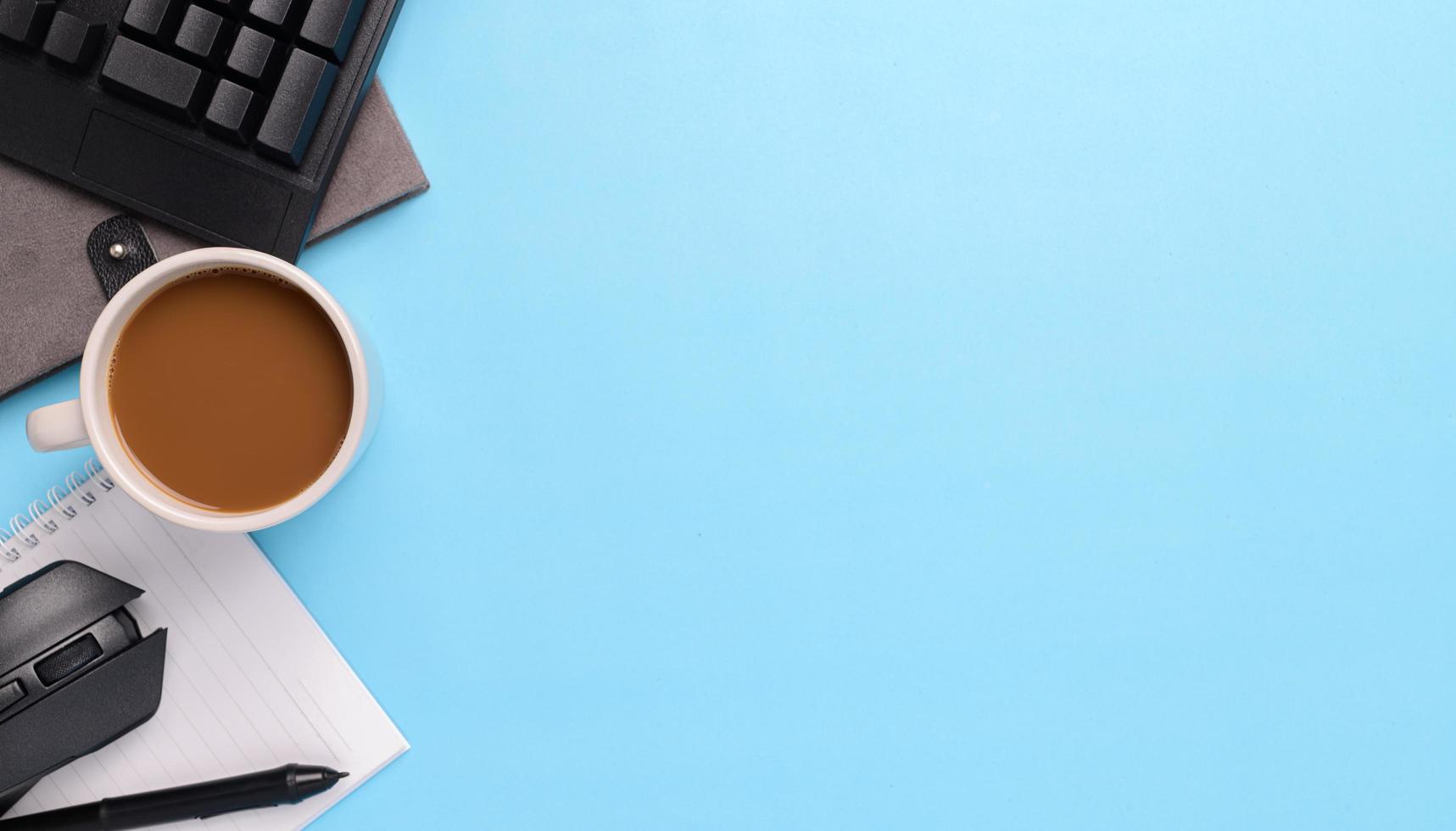 Lápiz electrónico, ratón, portátil, taza de café sobre fondo azul. foto