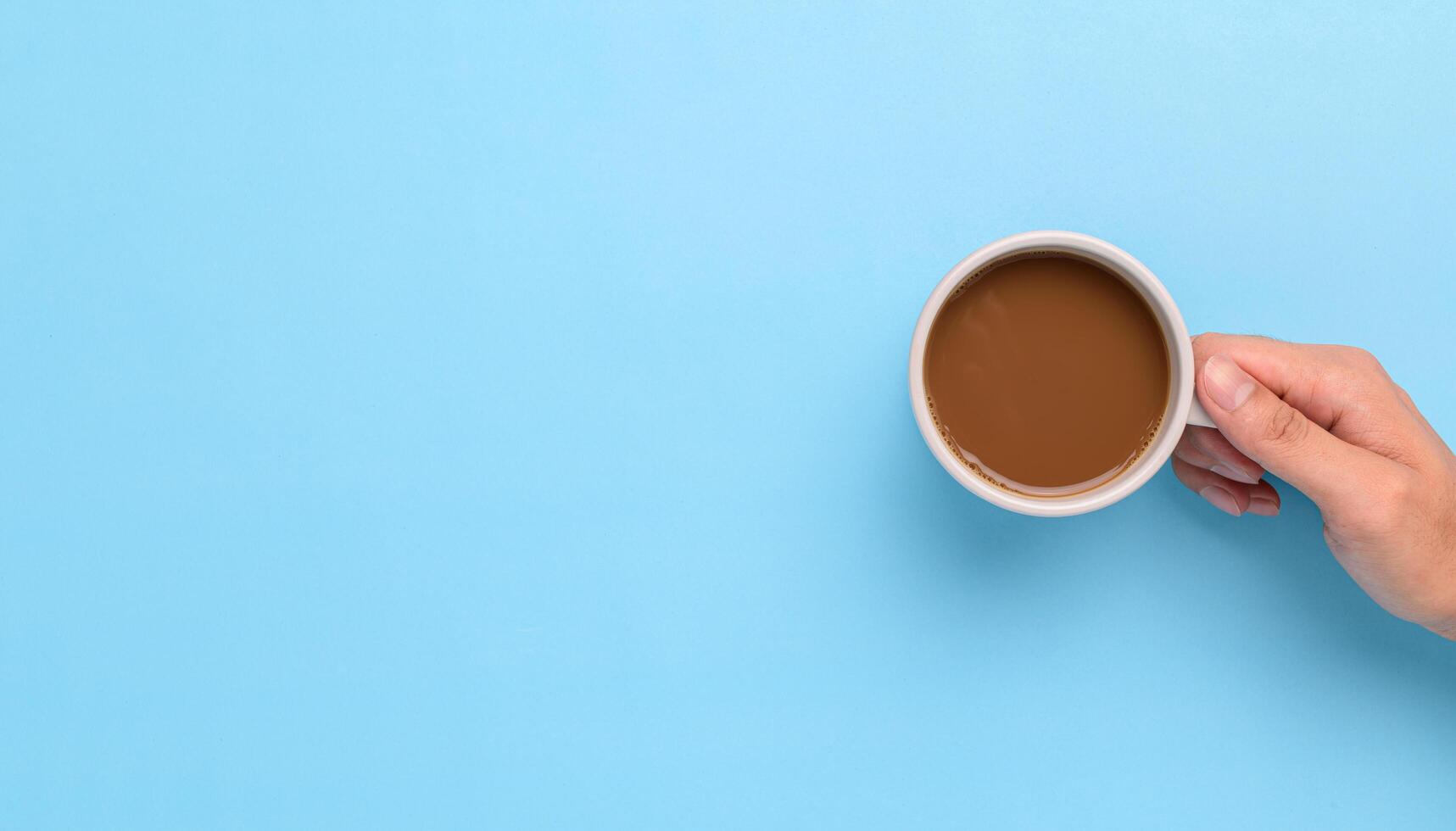 Mano sosteniendo una taza de café sobre un fondo azul. foto