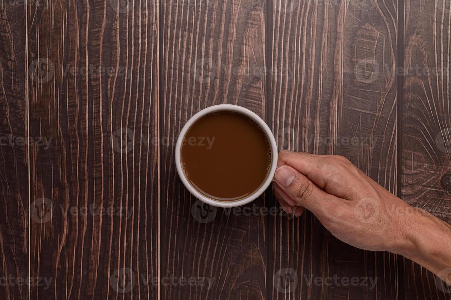 A person holding a cup of coffee on a wooden table photo