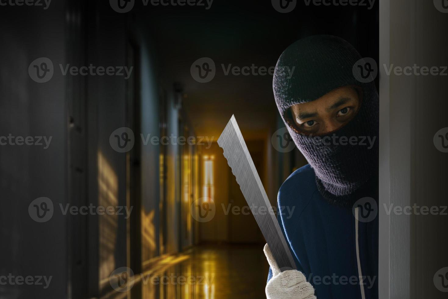 Masked robber with knife hiding behind the door photo