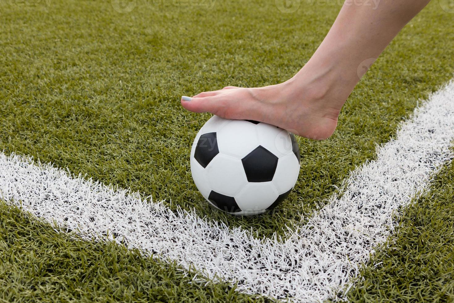 Girl's foot on the soccer ball on green field morning photo