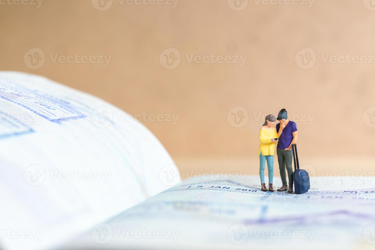 Miniature people couple standing on passport with immigration stamped photo